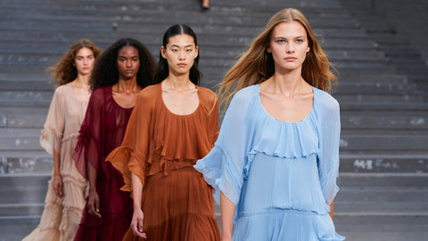 AI Fashion Four models walking down a runway wearing different colored dresses.